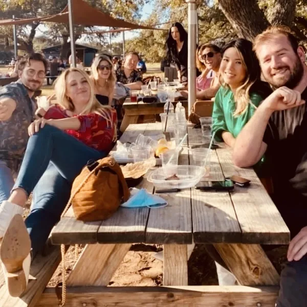 Group enjoying craft beer at an Austin brewery patio picnic table during a party bus brewery tour