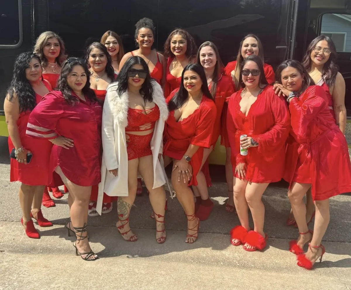 Bride tribe in matching red outfits with bride in white posing by party bus