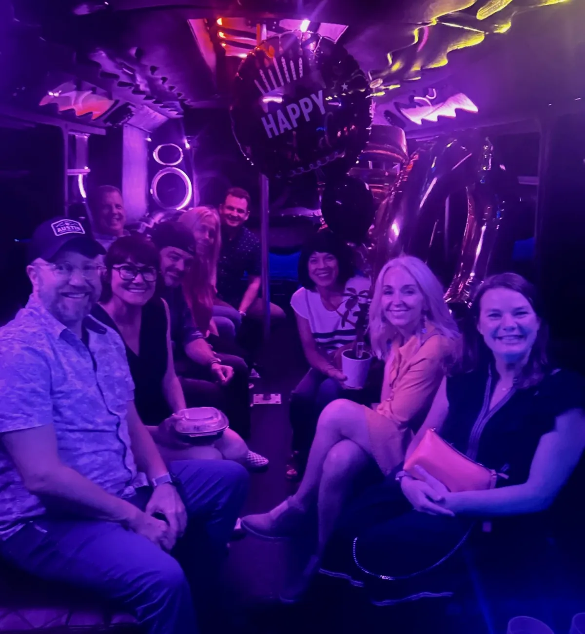 Friends celebrating a birthday on an Austin party bus with Happy Birthday balloons and purple lights