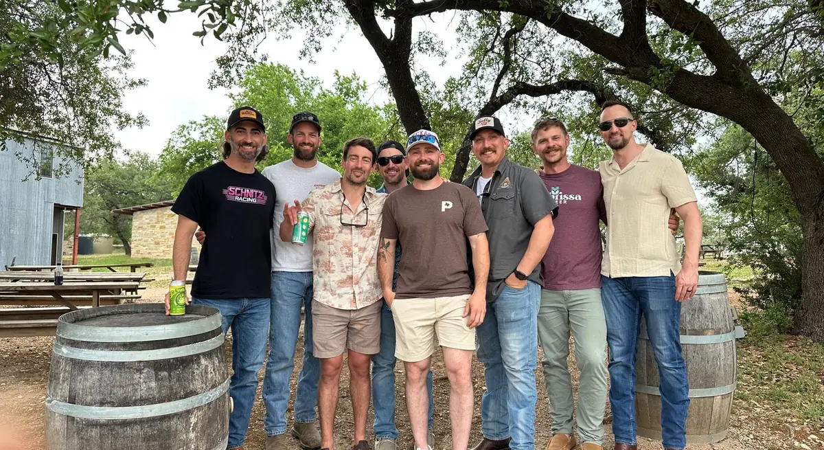 Group of friends at a Texas Hill Country winery with wine barrels and oak trees